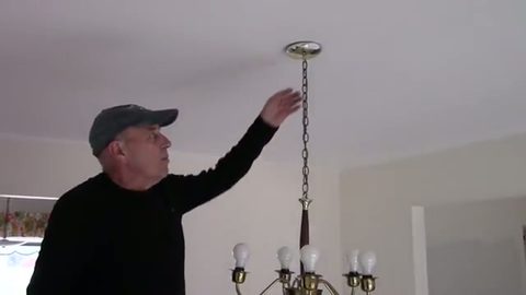 a man reaching up to detach a brass ceiling light fixture, face visible