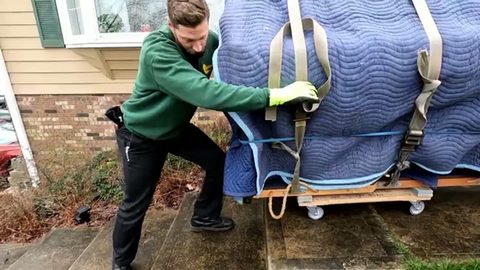 mover cinching a tension strap on a wrapped upright piano on a wheeled piano board, face visible