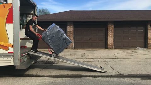 professional mover wheeling wrapped furniture down the truck ramp on a hand truck, face visible