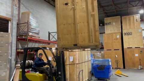 forklift hoisting a tall wooden storage vault in a moving warehouse, face visible