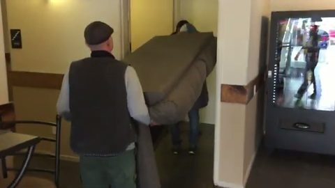 two movers carrying a couch down a hallway