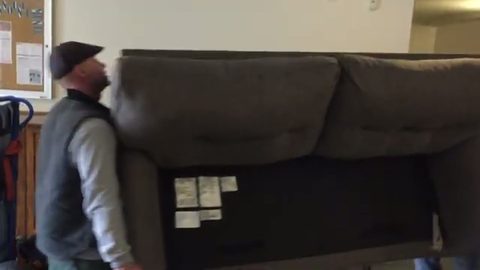 mover carrying a couch through an apartment building interior, face visible